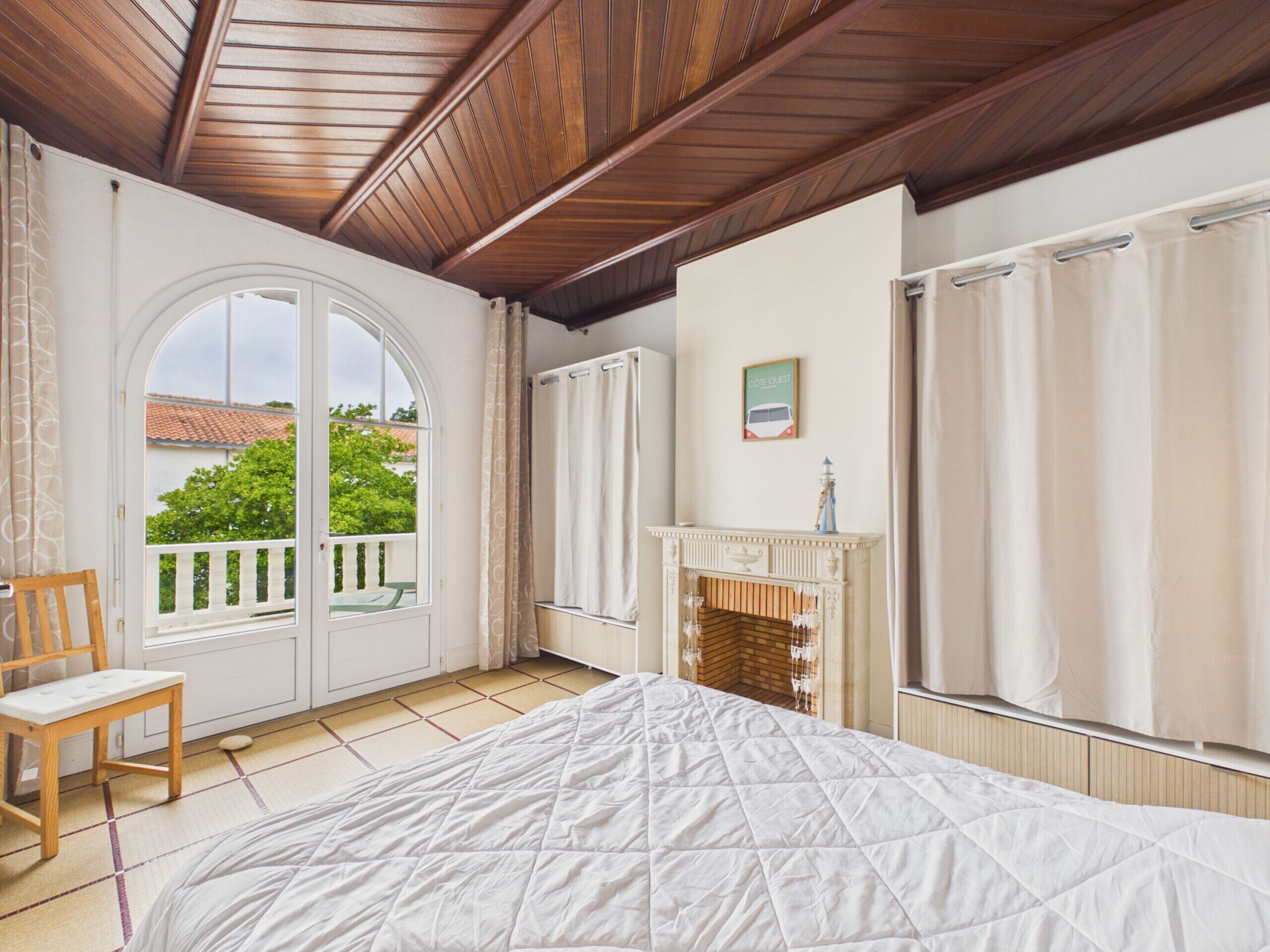 A bedroom with a bed, a chair, a fireplace, and a view of the outside.