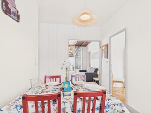 A dining area with a table set for two, chairs, a hanging light fixture, and a doorway leading to another room. - Beach 100m away, apartment with terrace for 4 (Longeville-sur-Mer)