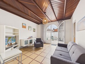 A living room with a sofa, a TV, a cabinet, and a ceiling with wooden beams. - Beach 100m away, apartment with terrace for 4 (Longeville-sur-Mer)