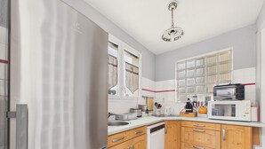 A kitchen with a refrigerator, microwave, sink, wooden cabinets, and a window with curtains. - Beach 100m away, apartment with terrace for 4 (Longeville-sur-Mer)