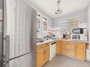 A kitchen with a refrigerator, microwave, sink, wooden cabinets, and a window with curtains. - Beach 100m away, apartment with terrace for 4 (Longeville-sur-Mer)