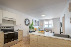 Eine moderne Küche mit weißen Schränken, einem eingebauten Backofen, einer großen Kochinsel mit Spüle und einem Essbereich mit Tisch für zwei Personen.