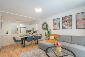 Ein modernes Wohnzimmer mit einem grauen Sofa, einem Couchtisch und einem Essbereich mit Tisch für vier Personen.