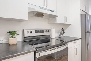 A modern kitchen with stainless steel appliances, white cabinetry, and a potted plant. - Elegant 3BR- Concordia- Indoor Parking / AC (Montréal)