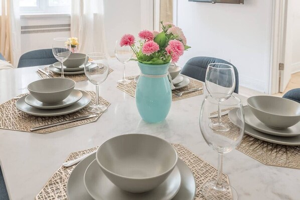 A dining table set with plates, bowls, and wine glasses, accompanied by a vase of flowers. - Elegant 3BR- Concordia- Indoor Parking / AC (Montréal)