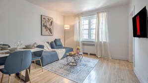 Una sala de estar moderna con sofá, mesa de comedor, sillas, alfombra y ventana con cortinas.