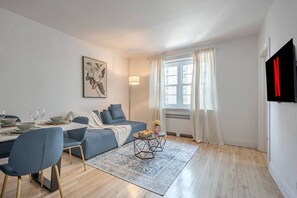 A modern living room with a sofa, dining table, and chairs, a rug, and a window with curtains. - Elegant 3BR- Concordia- Indoor Parking / AC (Montréal)