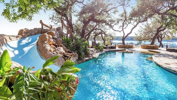A pool area with a rock waterfall, lounge chairs, and a view of the sea. - Lakeside House | Waterfront escape in Austin with resort-style pool (Austin)