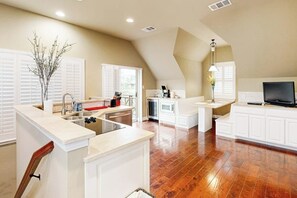 A kitchen with white cabinetry, a central island with a sink, and a dining area with a TV. - Countryside 3-story home with game room, WFH office & guest house with kitchen (Volente)