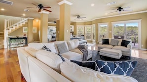 A spacious living area with a large sofa, a dining table, and a staircase leading to an upper level. - Countryside 3-story home with game room, WFH office & guest house with kitchen (Volente)