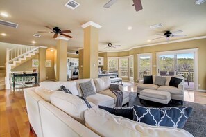 A spacious living area with a large sofa, a dining table, and a staircase leading to an upper level. - Countryside 3-story home with game room, WFH office & guest house with kitchen (Volente)