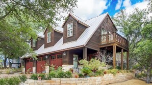 A two-story wooden house with a covered porch and a landscaped garden. - Countryside 3-story home with game room, WFH office & guest house with kitchen (Volente)