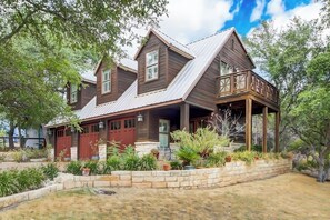 A two-story wooden house with a covered porch and a landscaped garden. - Countryside 3-story home with game room, WFH office & guest house with kitchen (Volente)
