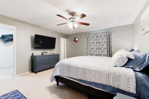 Ein Schlafzimmer mit einem Bett, einem Deckenventilator, einem Fernseher, einer Kommode und einer Wand mit einer Flagge.