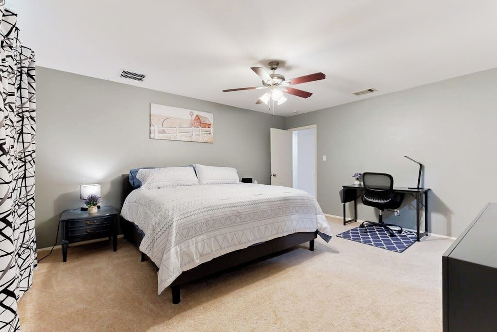 Ein Schlafzimmer mit Bett, Schreibtisch, Stuhl, Deckenventilator und Wandbild.