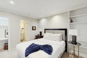 Ein Hotelzimmer mit Bett, Nachttischen, einem Bücherregal und einer Tür zu einem Badezimmer.