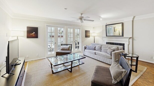A living room with a sofa, armchair, glass coffee table, TV, fireplace, and ceiling fan. - Charming, dog-friendly townhouse w/private gas grill, patio, & near downtown (Austin)