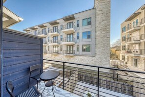 A balcony with a table and chairs, overlooking a modern apartment building with balconies.