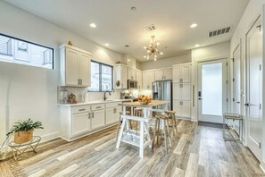 A modern kitchen with white cabinetry, a central island with stools, and a chandelier.