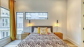 A bedroom with a bed, two bedside tables, a window with curtains, and a wall-mounted TV.