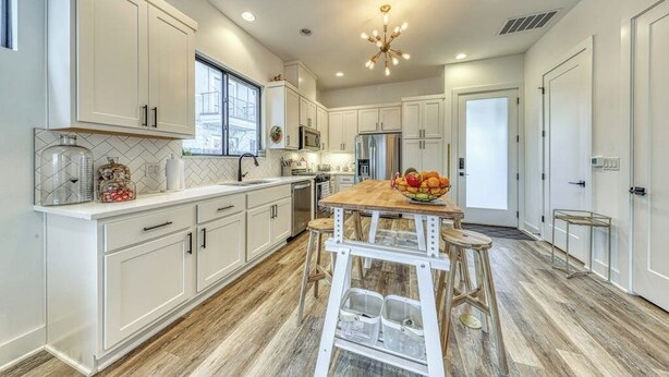A modern kitchen with white cabinetry, a wooden island, and a central light fixture.