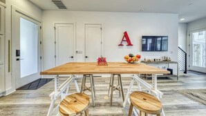 A modern kitchen with a wooden table, stools, and a fruit bowl.