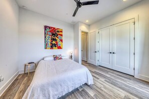A bedroom with a bed, a ceiling fan, a colorful artwork, a nightstand, and a wardrobe.