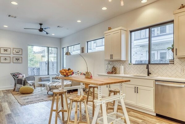 A modern kitchen with wooden stools, a dining table, and a large window.