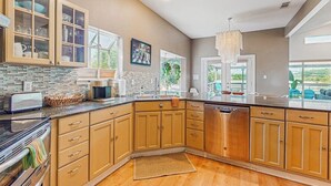 A modern kitchen with wooden cabinets, a granite countertop, and a built-in dishwasher. - Contemporary dog-friendly house w/ private gas grill, hot tub, & outdoor pool (Austin)