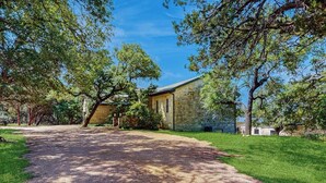 A stone building with a gravel driveway and surrounding greenery. - Contemporary dog-friendly house w/ private gas grill, hot tub, & outdoor pool (Austin)