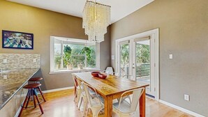 A modern kitchen with a wooden table, white chairs, a chandelier, and a large window. - Contemporary dog-friendly house w/ private gas grill, hot tub, & outdoor pool (Austin)