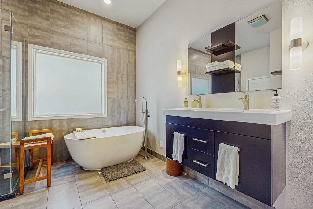 Ein modernes Badezimmer mit einer freistehenden Badewanne, einem Waschtisch mit Spiegel und einer Duschkabine aus Glas.