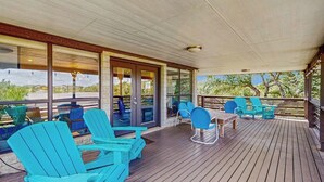 A covered outdoor deck with wooden flooring, glass doors, and blue Adirondack chairs. - Contemporary dog-friendly house w/ private gas grill, hot tub, & outdoor pool (Austin)