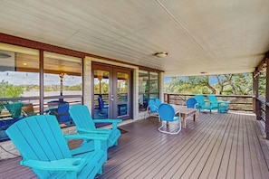 Eine überdachte Terrasse im Freien mit Holzboden, Glastüren und blauen Adirondack-Stühlen.