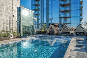 Une piscine entourée de parois en verre, un bâtiment moderne doté de balcons et un ciel dégagé.