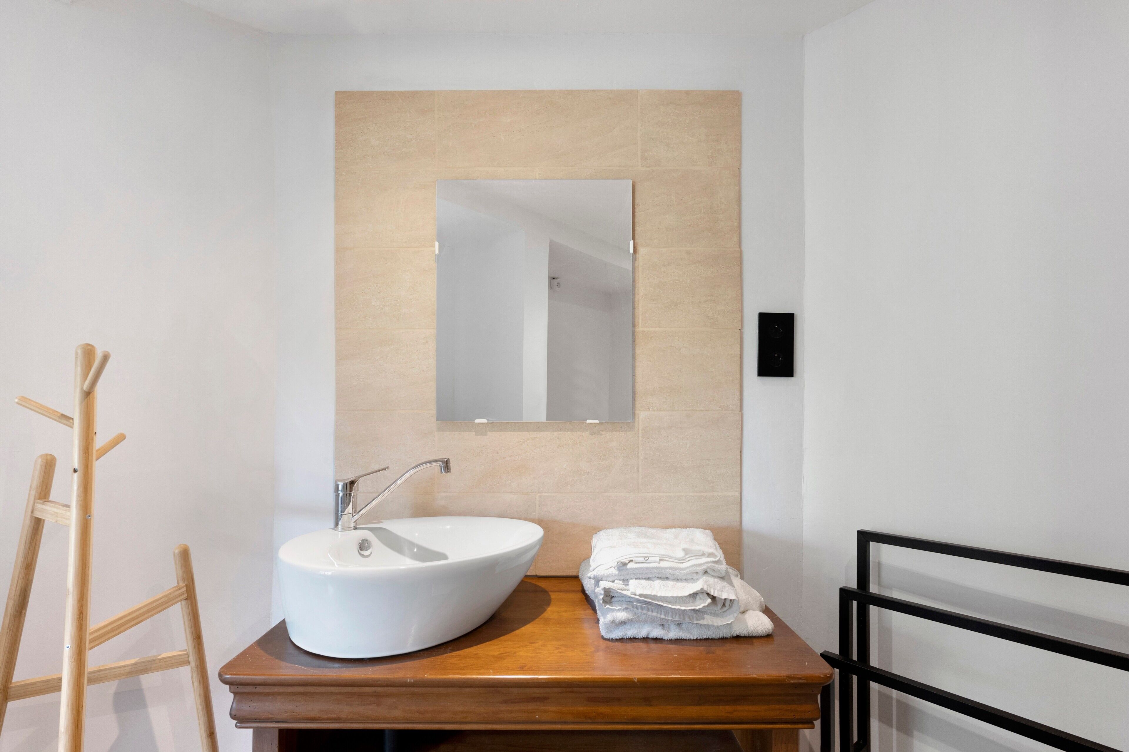 A bathroom with a white sink, a wooden vanity, a mirror, and a towel rack.