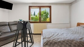 Quarto com cama, sofá, mesa e janela com vista para árvores.