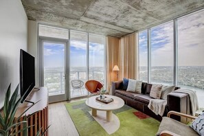 Ein modernes Wohnzimmer mit großem Fenster, Flachbildfernseher, Sofa, Couchtisch und einer Pflanze.