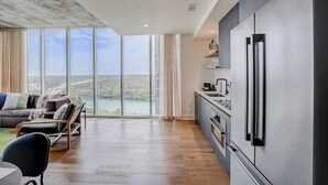 Cozinha moderna com uma geladeira grande, área de refeições com mesa e cadeiras, e vista para a água por grandes janelas.