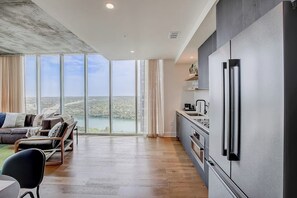 Eine moderne Küche mit einem großen Kühlschrank, einem Essbereich mit Tisch und Stühlen und Blick auf ein Gewässer durch große Fenster.