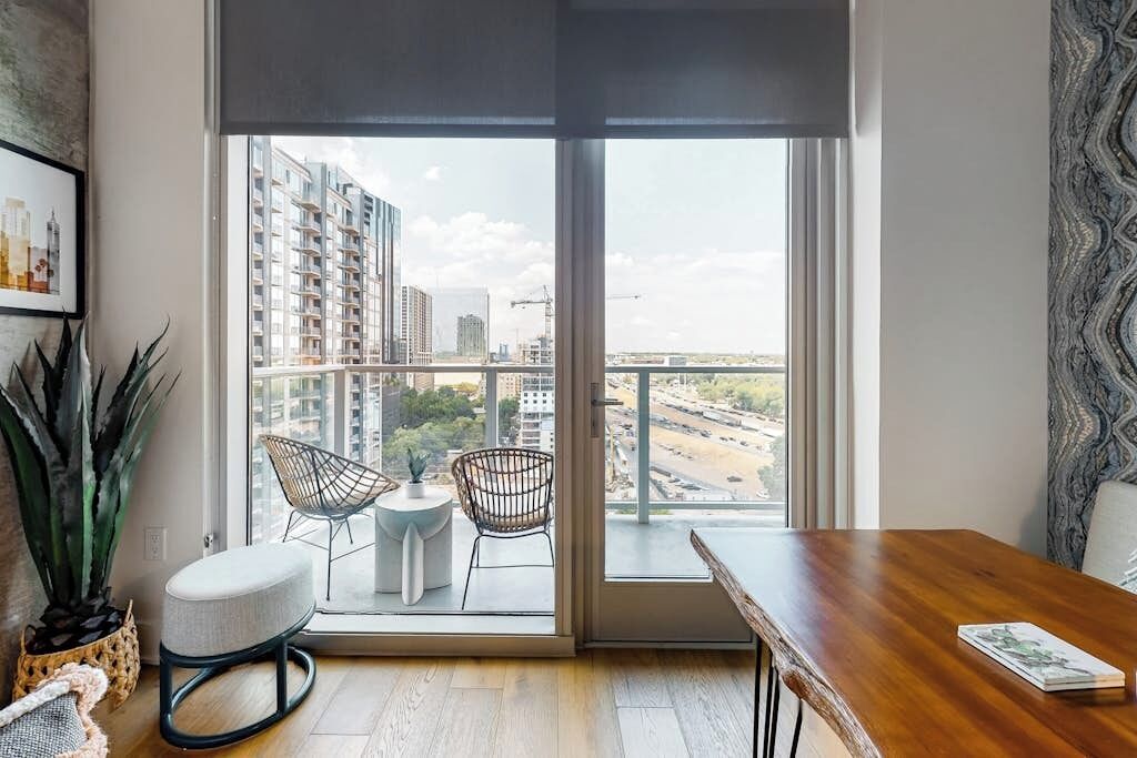 Un appartement moderne doté d’une grande porte-fenêtre coulissante, de deux fauteuils, d’une petite table et d’un bureau en bois.