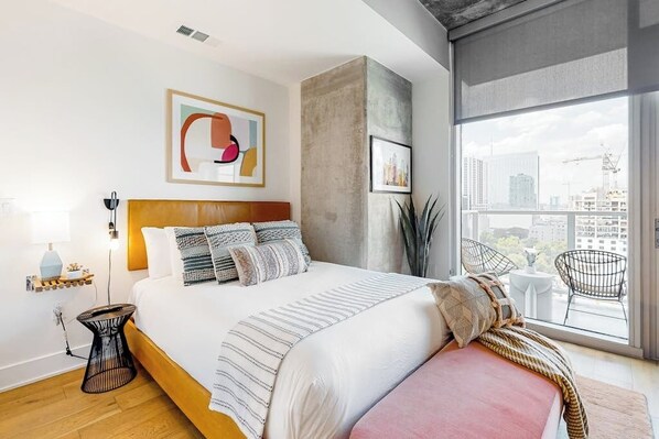 Ein modernes Schlafzimmer mit einem großen Bett, Blick auf die Stadt und einer Wand mit Betonoptik.