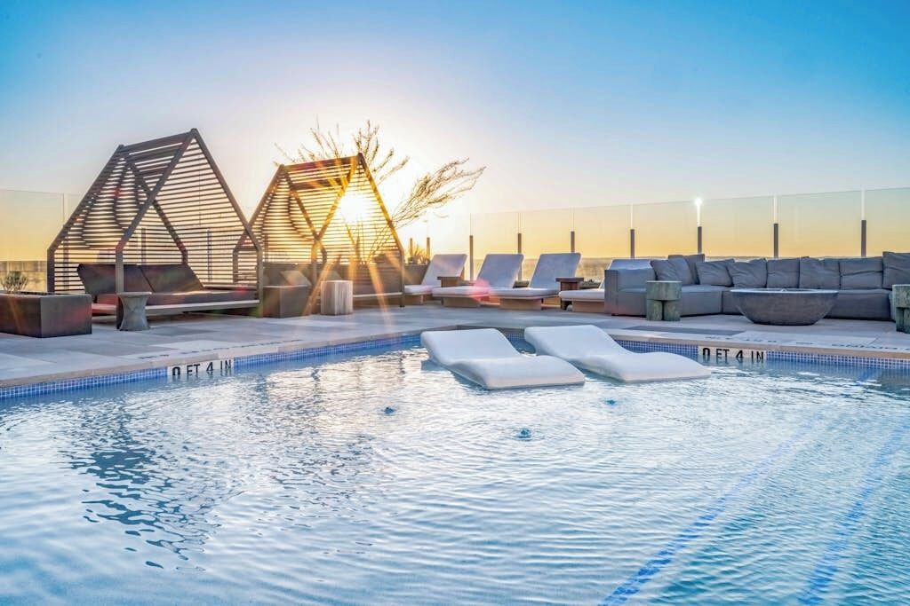 Een zwembad op het dak met ligbedden, een jacuzzi en uitzicht op de ondergaande zon.