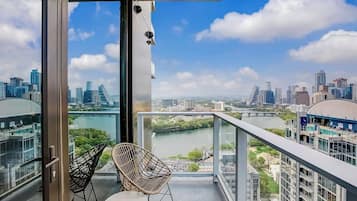 A balcony with a city view, two wicker chairs, and a table.