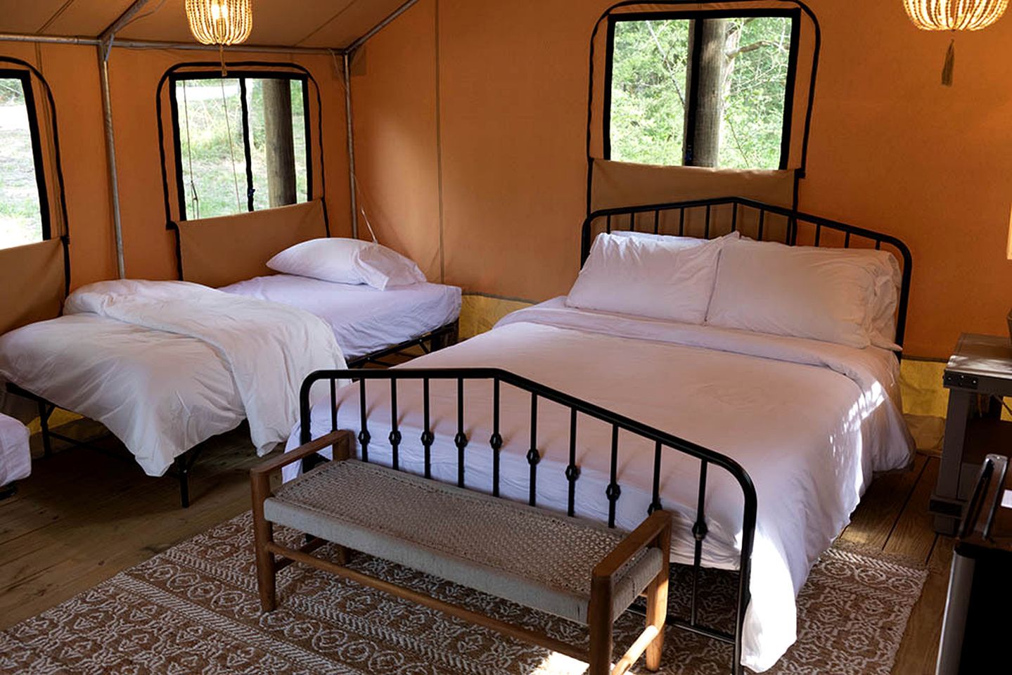 A tent-style room with two beds, a bench, and a small table.