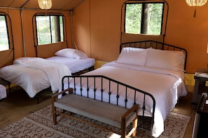 A tent-style room with two beds, a bench, and a small table.