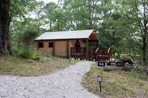 Un chalet rustique, accessible par un chemin de gravier, et entouré d’arbres.