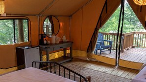 A tent with a bed, a dresser, and a chair on a deck with a view of trees. - Great Small Group Safari Tent in Livingston, Texas (Livingston)