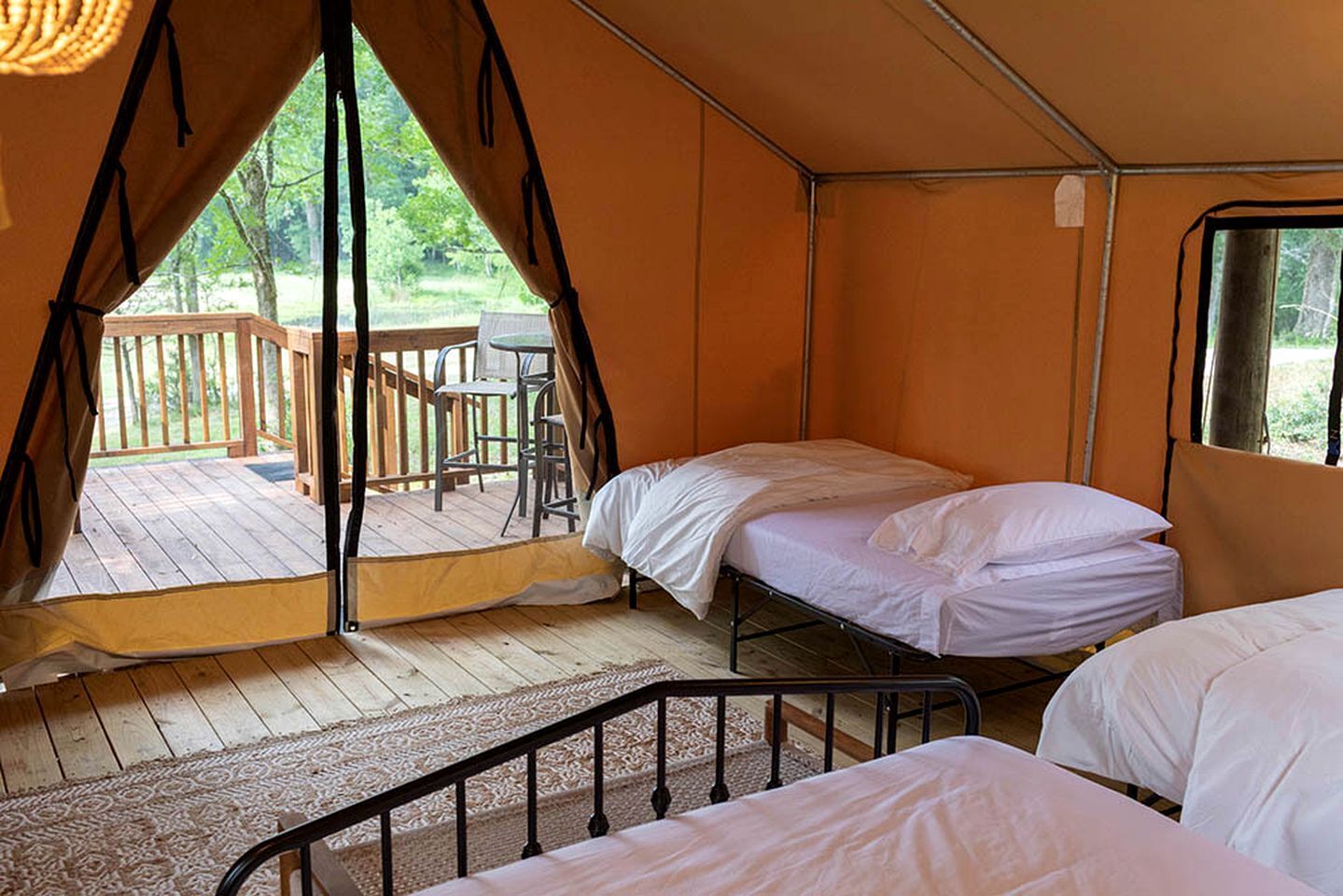 A tent with two beds, a wooden deck, and a table outside.