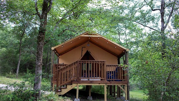 A wooden cabin with a balcony, surrounded by trees. - Great Small Group Safari Tent in Livingston, Texas (Livingston)